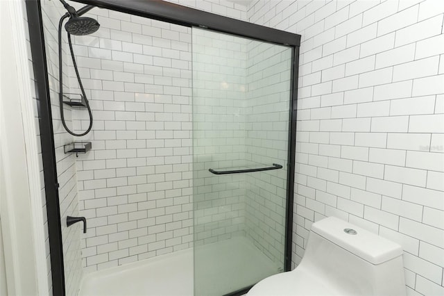 bathroom featuring a shower with shower door, tile walls, and toilet