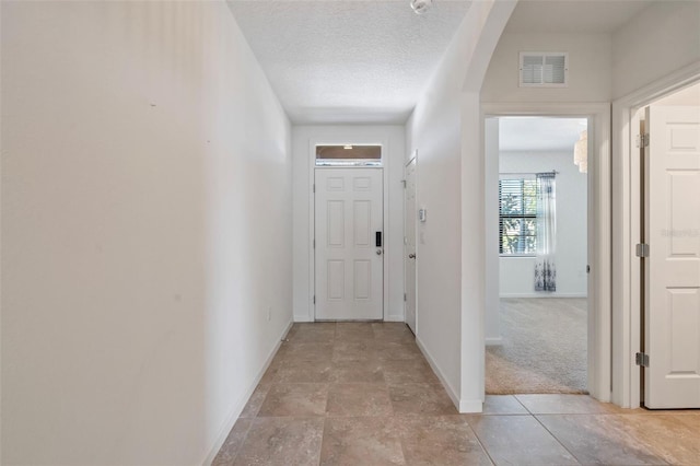 hallway with light carpet and a textured ceiling