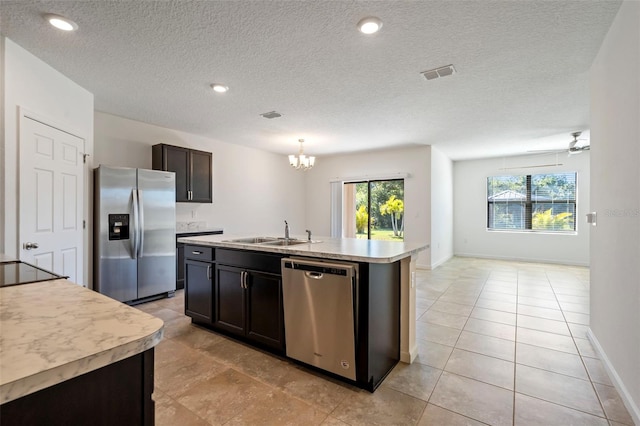 kitchen featuring ceiling fan with notable chandelier, stainless steel appliances, sink, pendant lighting, and an island with sink