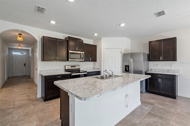 kitchen with dark brown cabinetry, sink, a center island with sink, and appliances with stainless steel finishes