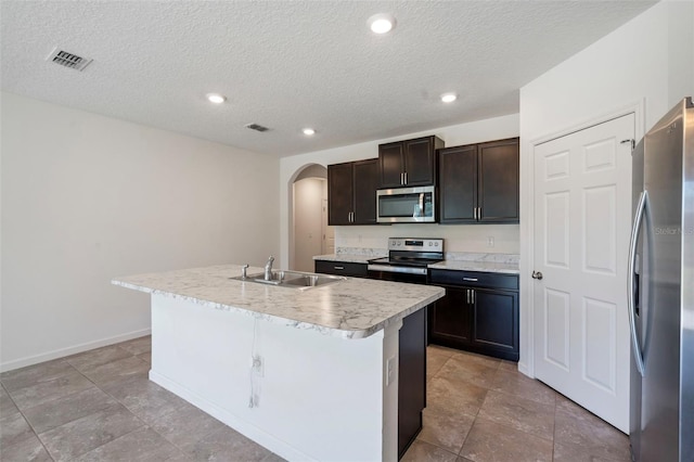 kitchen with a center island with sink, sink, stainless steel appliances, and a textured ceiling