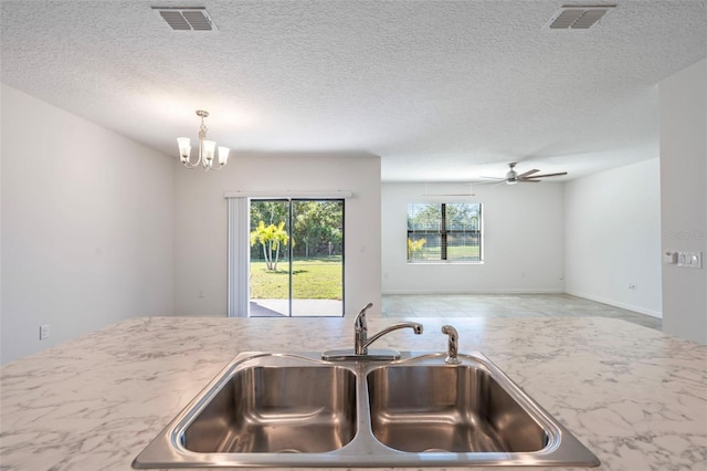 kitchen with a textured ceiling, sink, decorative light fixtures, and ceiling fan with notable chandelier