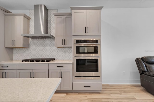 kitchen featuring appliances with stainless steel finishes, wall chimney range hood, gray cabinets, and decorative backsplash