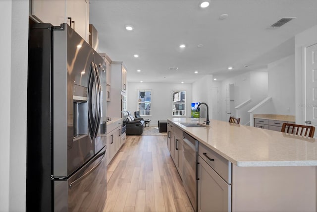 kitchen with a large island, appliances with stainless steel finishes, light wood-type flooring, a breakfast bar, and sink