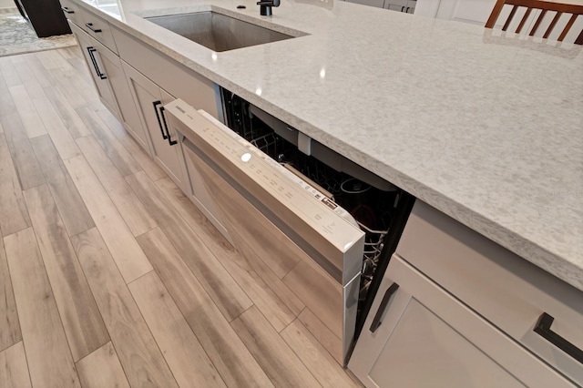 room details with sink, light wood-type flooring, white cabinetry, and light stone counters