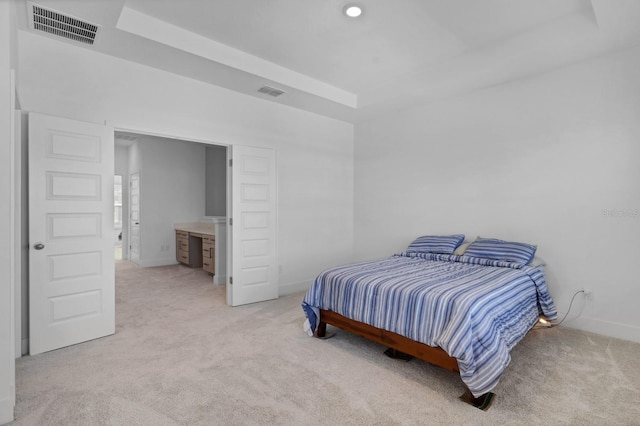 bedroom with ensuite bathroom, a raised ceiling, and light colored carpet