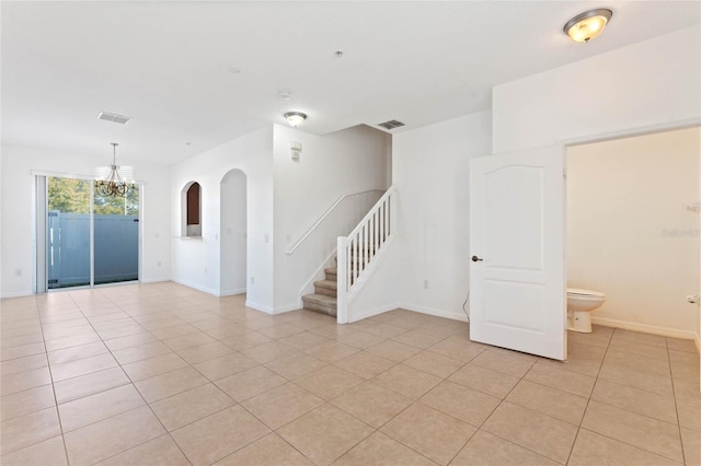 tiled spare room with a chandelier