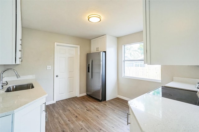 kitchen featuring light stone countertops, stainless steel refrigerator with ice dispenser, light wood-type flooring, sink, and white cabinets