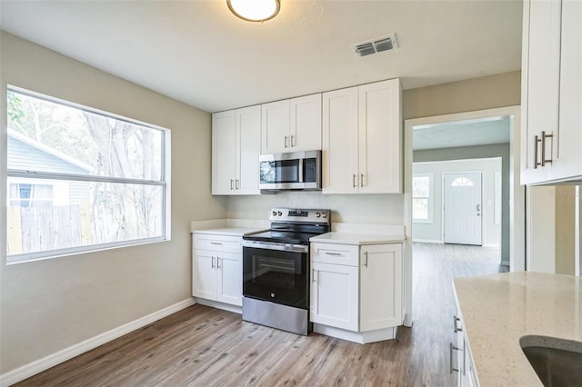 kitchen with light stone counters, white cabinets, light wood-type flooring, and appliances with stainless steel finishes