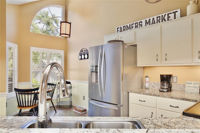 kitchen featuring stainless steel refrigerator with ice dispenser, sink, and light stone countertops