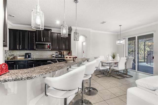 kitchen with a kitchen bar, backsplash, ornamental molding, light tile patterned floors, and decorative light fixtures