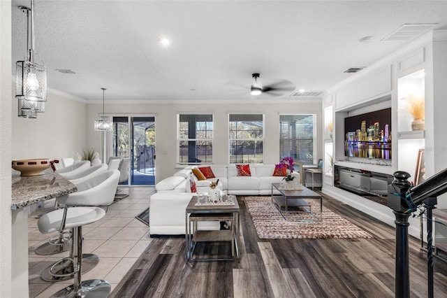 living room with hardwood / wood-style flooring, ceiling fan with notable chandelier, ornamental molding, and a textured ceiling