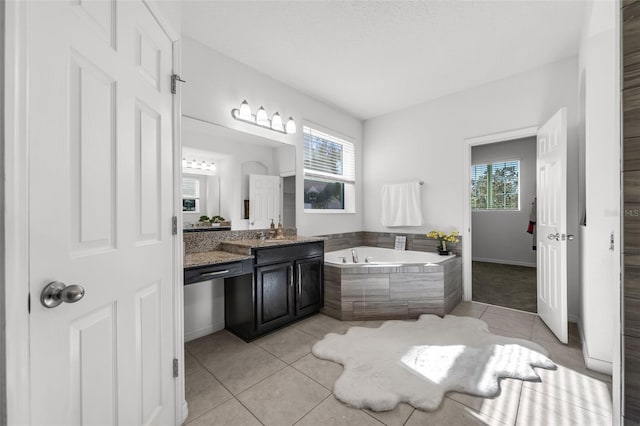 bathroom featuring tile patterned flooring, vanity, a healthy amount of sunlight, and tiled tub