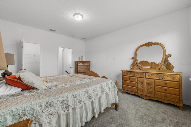 bedroom with a walk in closet, light carpet, a closet, and a textured ceiling