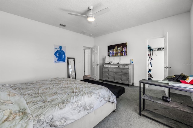 carpeted bedroom with a walk in closet, a textured ceiling, a closet, and ceiling fan