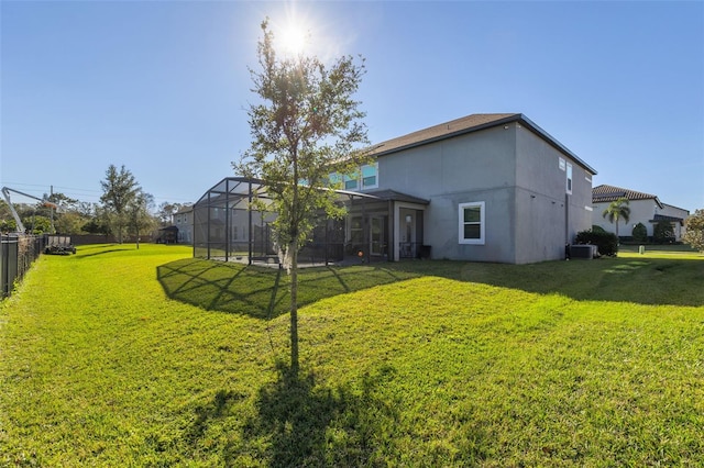 back of house featuring central AC unit, glass enclosure, and a yard