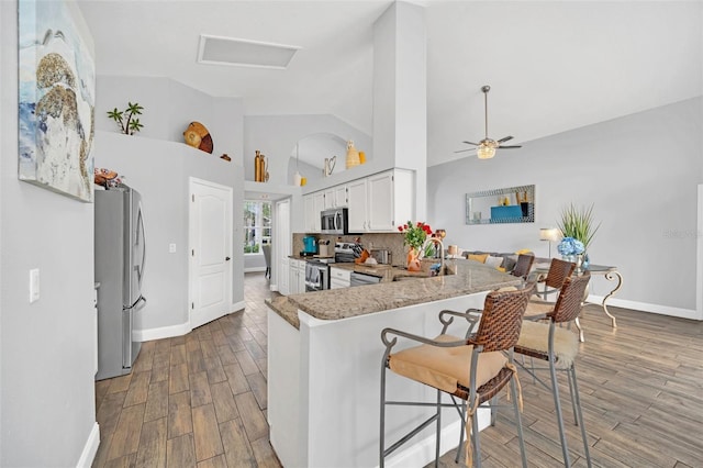 kitchen with kitchen peninsula, appliances with stainless steel finishes, white cabinets, a breakfast bar, and sink