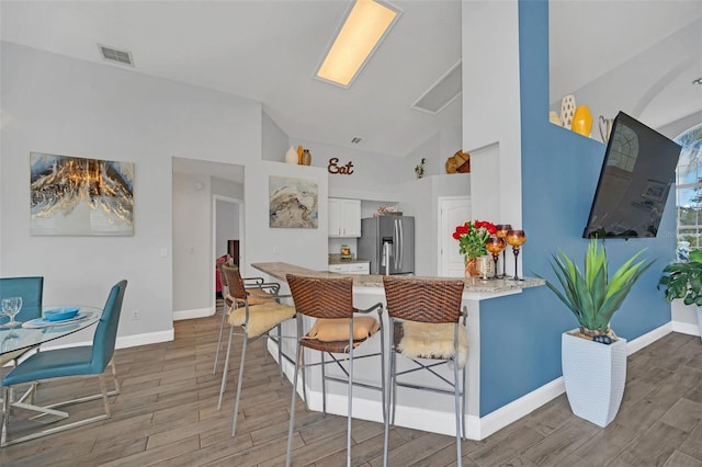 kitchen with white cabinets, stainless steel fridge with ice dispenser, kitchen peninsula, high vaulted ceiling, and a breakfast bar