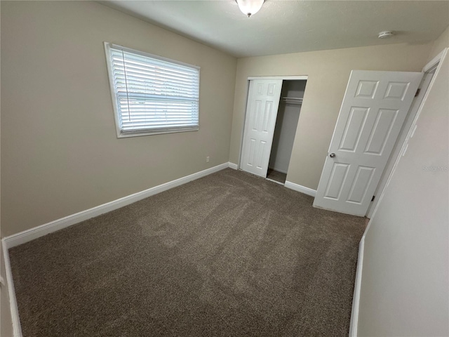 unfurnished bedroom with dark carpet and a closet