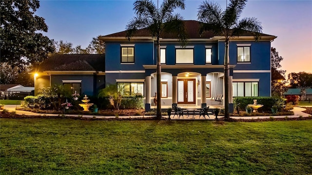 back house at dusk featuring a lawn and french doors