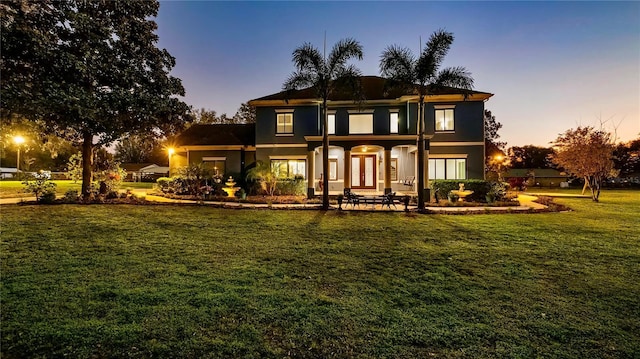 back house at dusk featuring a lawn