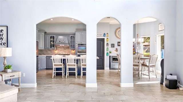 kitchen featuring a breakfast bar, gray cabinetry, double oven, custom range hood, and decorative backsplash