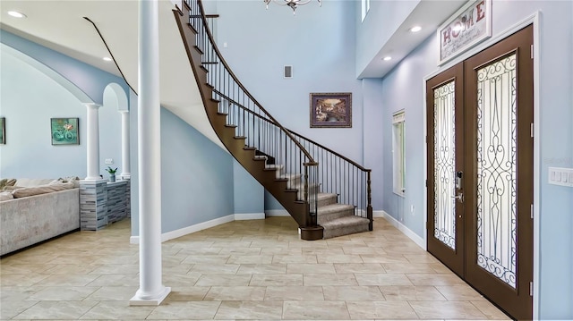 foyer featuring a towering ceiling, decorative columns, and french doors