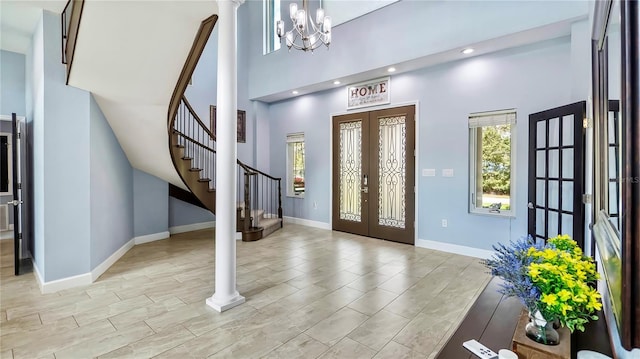 entrance foyer featuring a towering ceiling, light hardwood / wood-style floors, french doors, a chandelier, and ornate columns