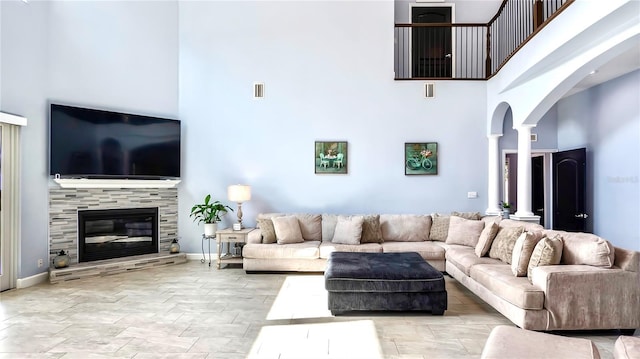 living room featuring a tiled fireplace, decorative columns, and a high ceiling