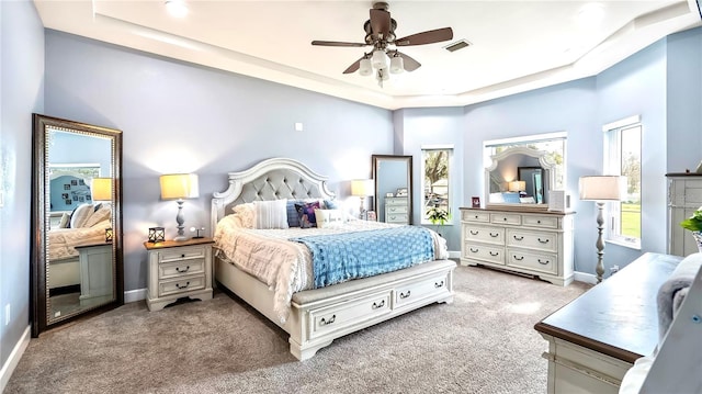 carpeted bedroom with ceiling fan and a tray ceiling