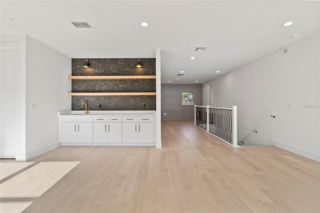 bar with sink, white cabinetry, and light hardwood / wood-style flooring