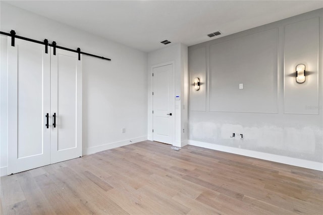 unfurnished bedroom featuring light wood-type flooring and a barn door