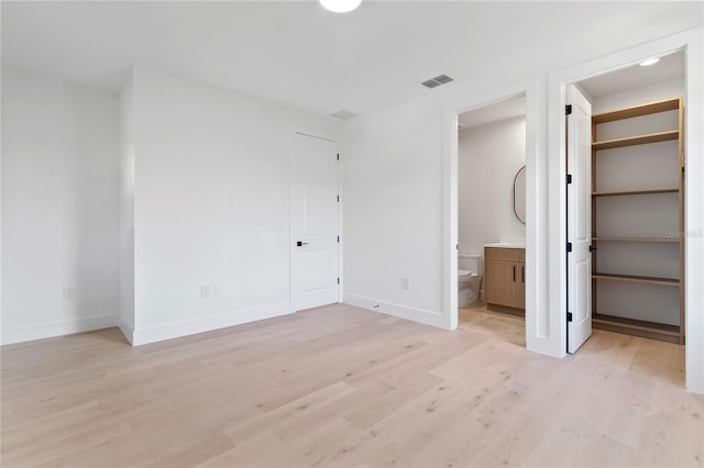 unfurnished bedroom featuring ensuite bathroom, a walk in closet, light wood-type flooring, and a closet