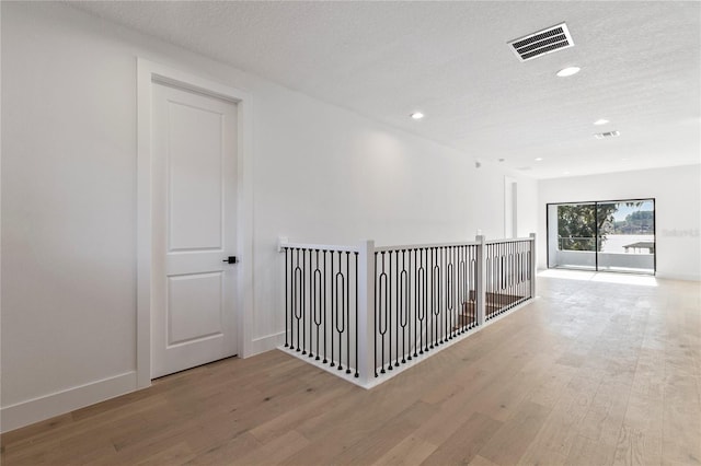 hall with a textured ceiling and light hardwood / wood-style flooring