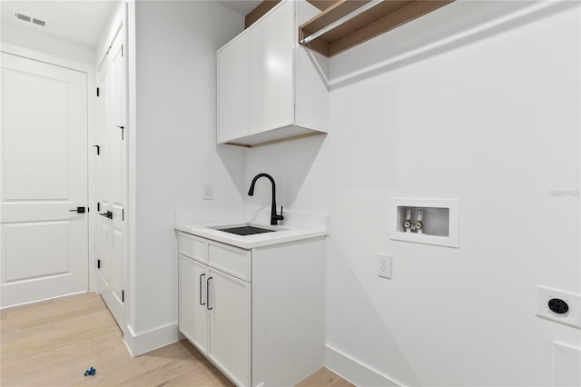 washroom with cabinets, electric dryer hookup, washer hookup, sink, and light hardwood / wood-style flooring