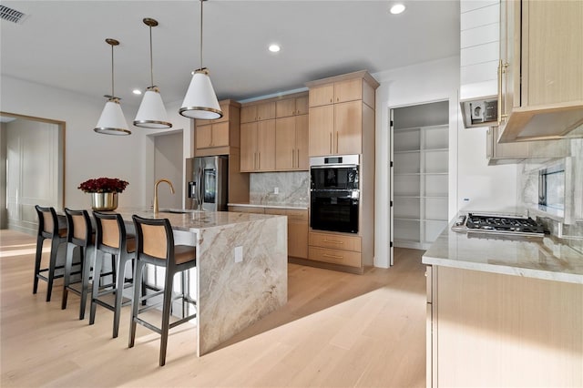 kitchen featuring sink, stainless steel appliances, light brown cabinetry, and hanging light fixtures