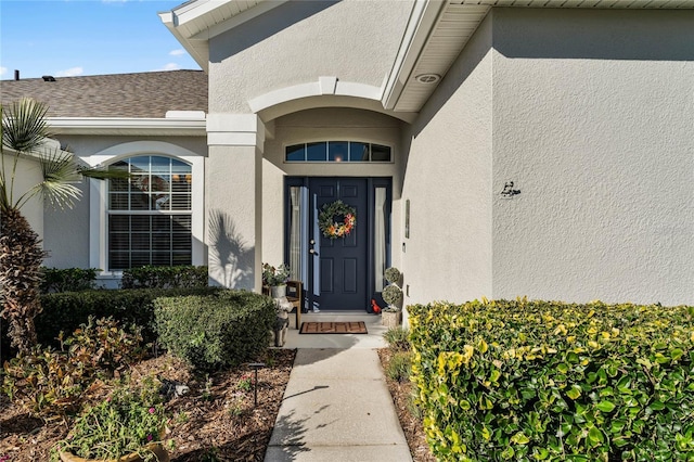 entrance to property featuring roof with shingles and stucco siding