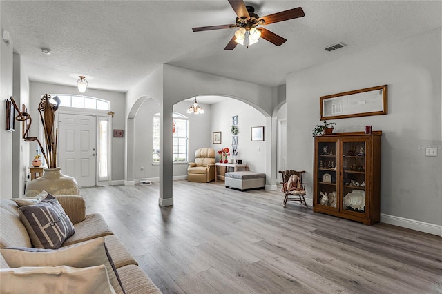 living room with ceiling fan with notable chandelier, light hardwood / wood-style flooring, and a textured ceiling