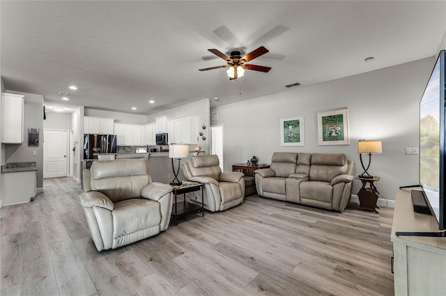 living room with a textured ceiling, ceiling fan, and light wood-type flooring