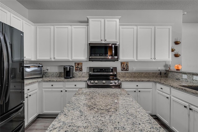 kitchen with light stone counters, a textured ceiling, stainless steel appliances, and white cabinets