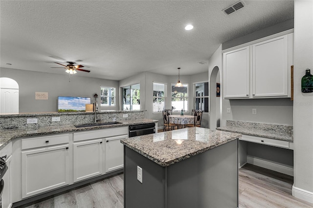 kitchen featuring white cabinetry, sink, hanging light fixtures, a center island, and light stone counters