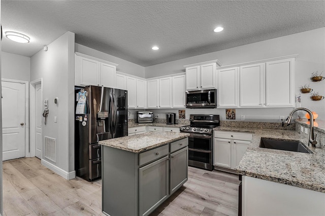 kitchen featuring appliances with stainless steel finishes, white cabinetry, sink, a center island, and a textured ceiling