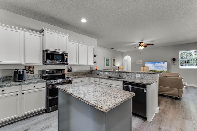 kitchen featuring arched walkways, open floor plan, a peninsula, stainless steel appliances, and a sink