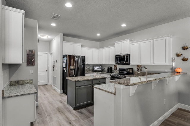 kitchen with light stone counters, stainless steel microwave, light wood-style floors, range with electric cooktop, and a peninsula