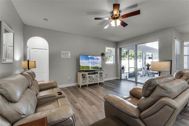 living area with arched walkways, wood finished floors, a ceiling fan, and baseboards