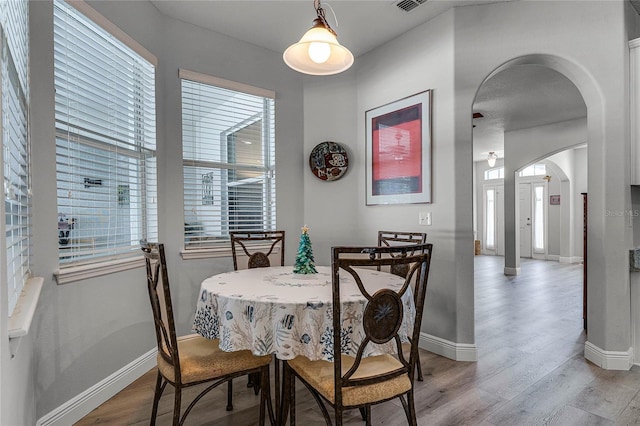 dining room featuring light wood-type flooring, baseboards, and arched walkways