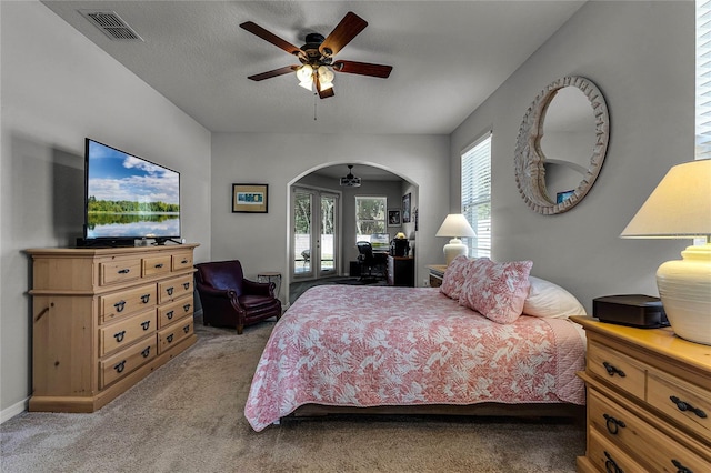 bedroom with arched walkways, french doors, light colored carpet, visible vents, and ceiling fan