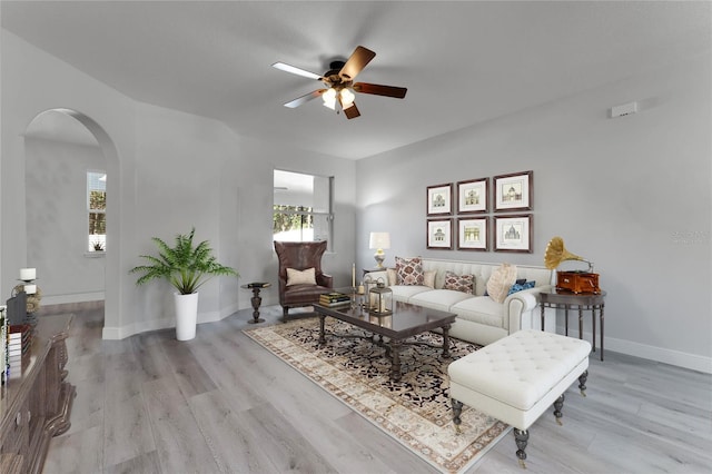 living room with arched walkways, baseboards, ceiling fan, and light wood finished floors