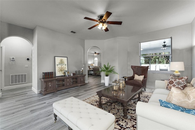 living room featuring arched walkways, ceiling fan, wood finished floors, and visible vents