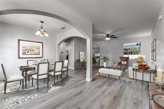 dining room featuring visible vents, arched walkways, a textured ceiling, light wood-style floors, and ceiling fan with notable chandelier